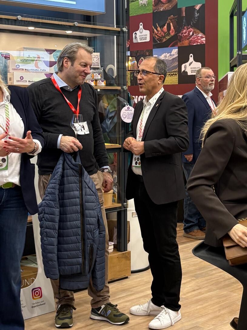 Eine Gruppe von Menschen in einem Raum, darunter Männer und Frauen in Anzügen, umgeben von Möbeln.