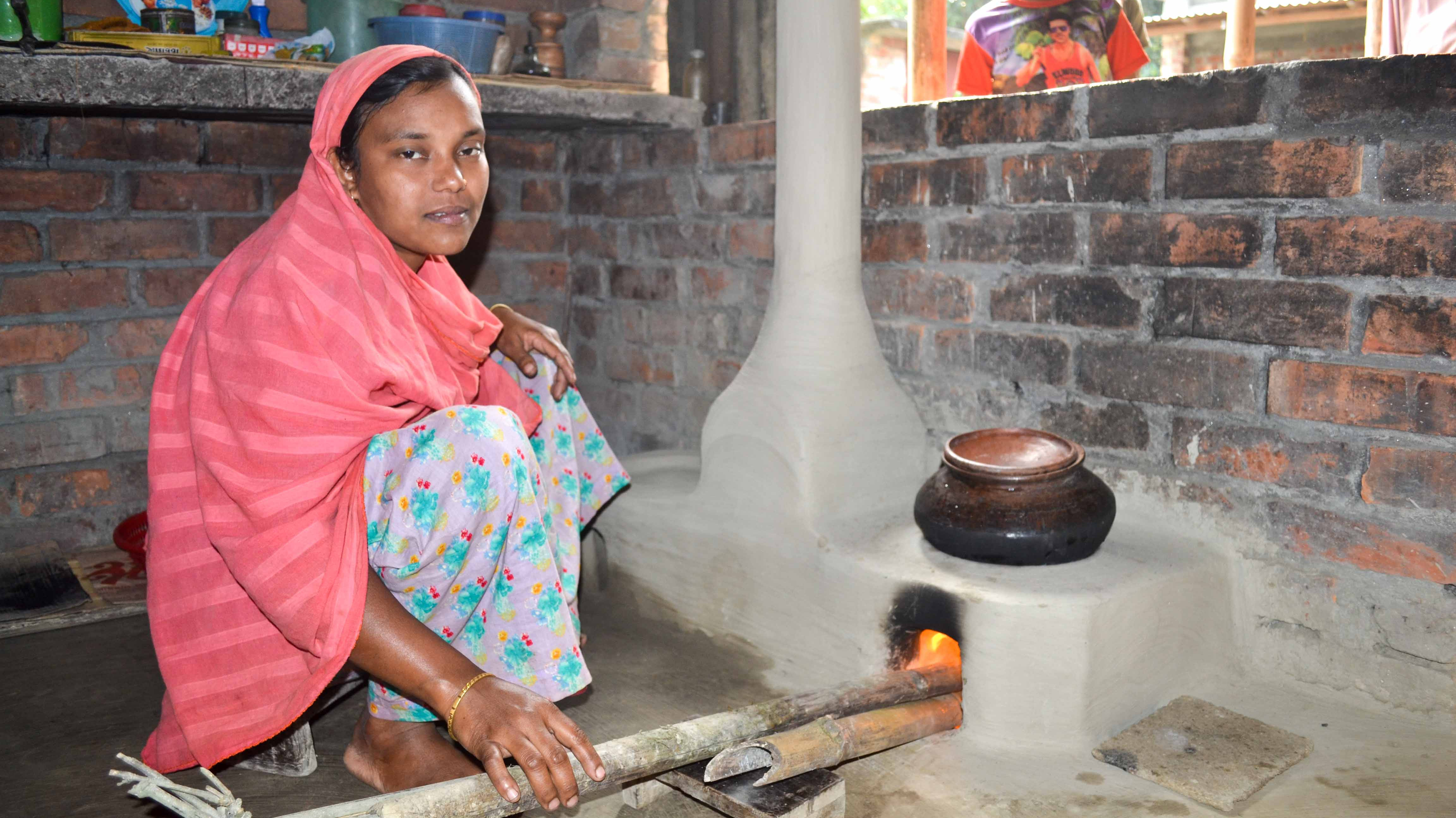 Frau in traditioneller Kleidung legt Holz in einem Holzofen nach