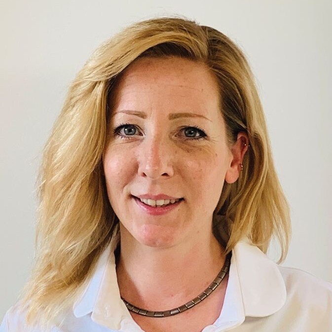 Eine Frau mit blonden Haaren und weißem Hemd lächelnd.