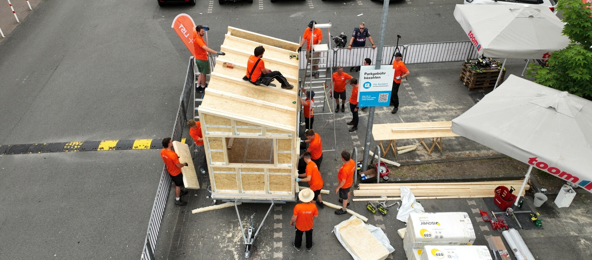Projekt Little Home Eine Gruppe von Personen in orangefarbenen Hemden beim Bau eines Hauses.