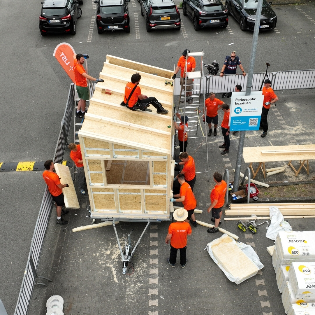 Eine Gruppe von Menschen in orangefarbenen Hemden beim Bau eines Hauses.